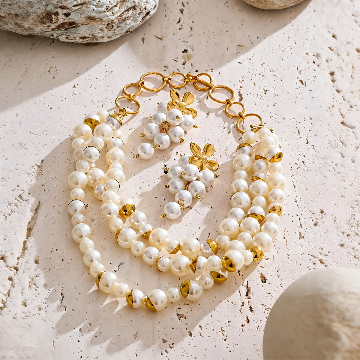 Layered pearl necklace and flower drop earrings set arranged on a warm stone surface