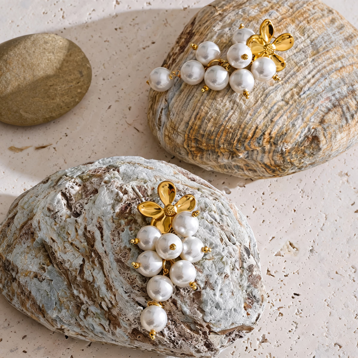 Pair of gold flower and simulated pearl drop earrings resting on stones