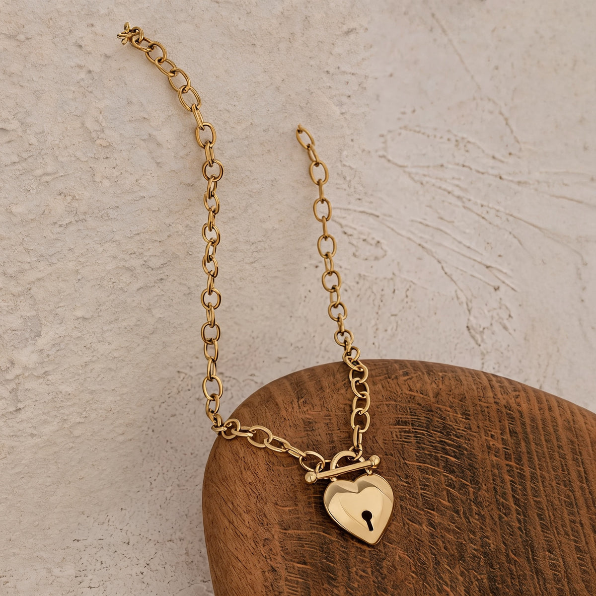 Gold Etta heart lock choker laid on a plaster surface with a wooden dome