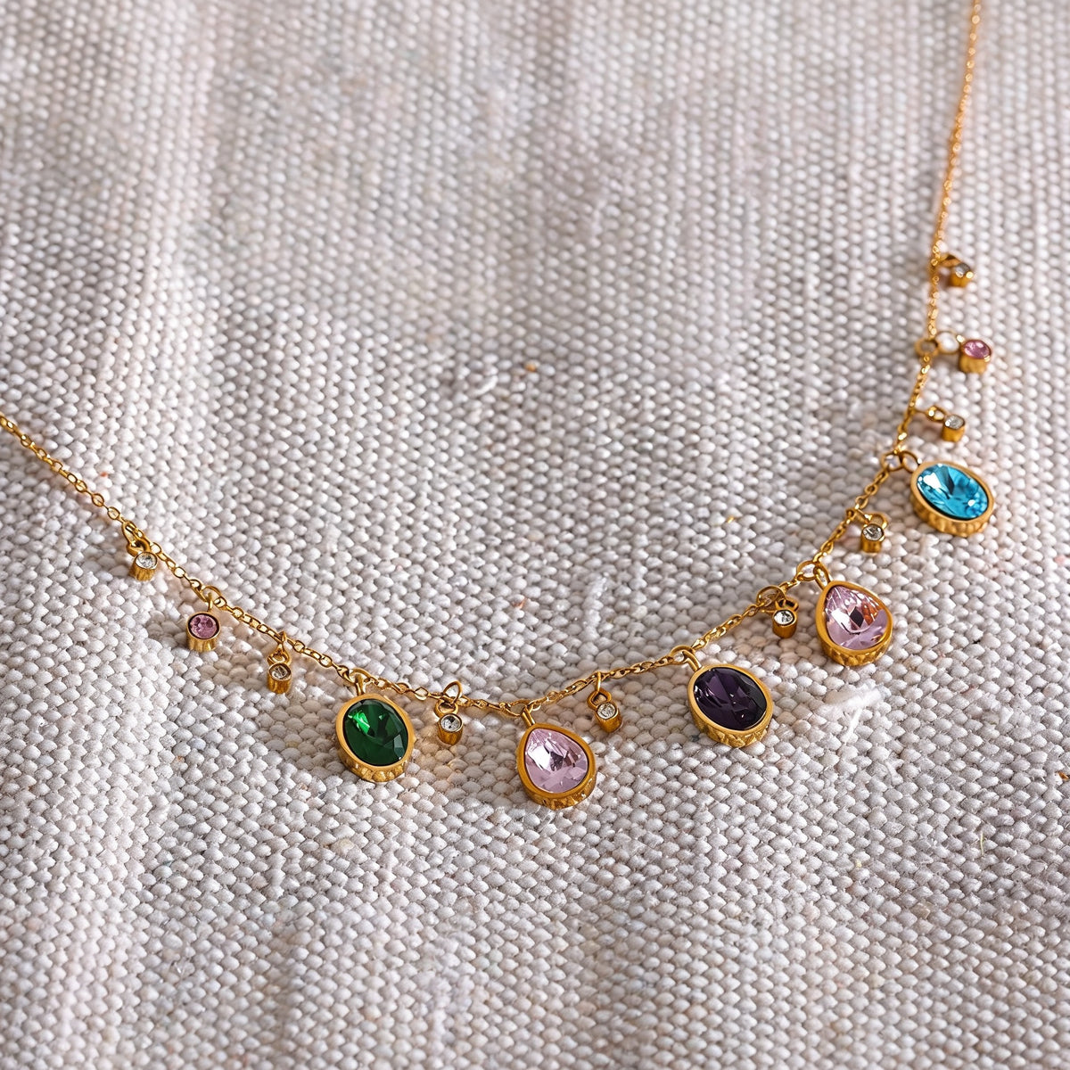 Fern Zirconia Necklace laid on cream linen, colored cubic zirconia charms