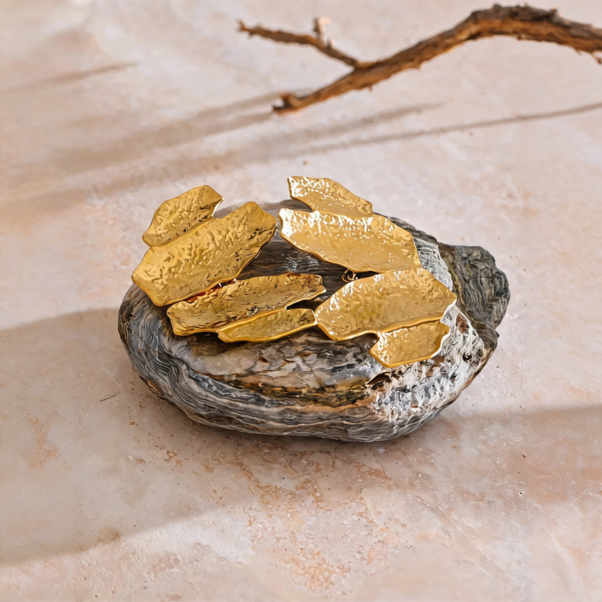 Faye hammered gold-tone drop earrings resting on a river stone