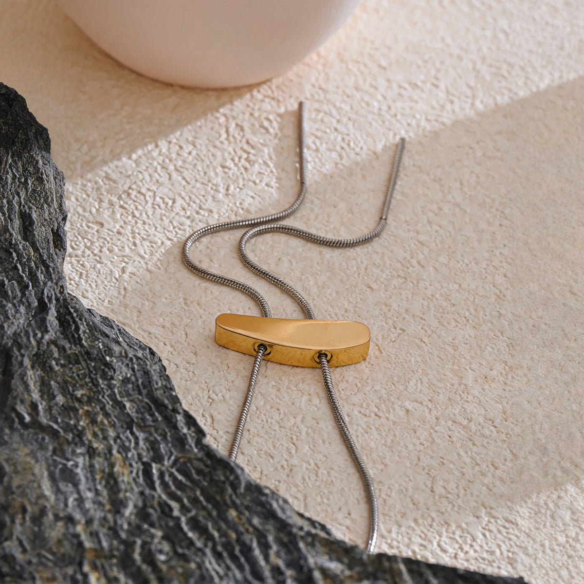 Marlow Long Chain Necklace laid flat on sand-toned plaster beside a slate stone