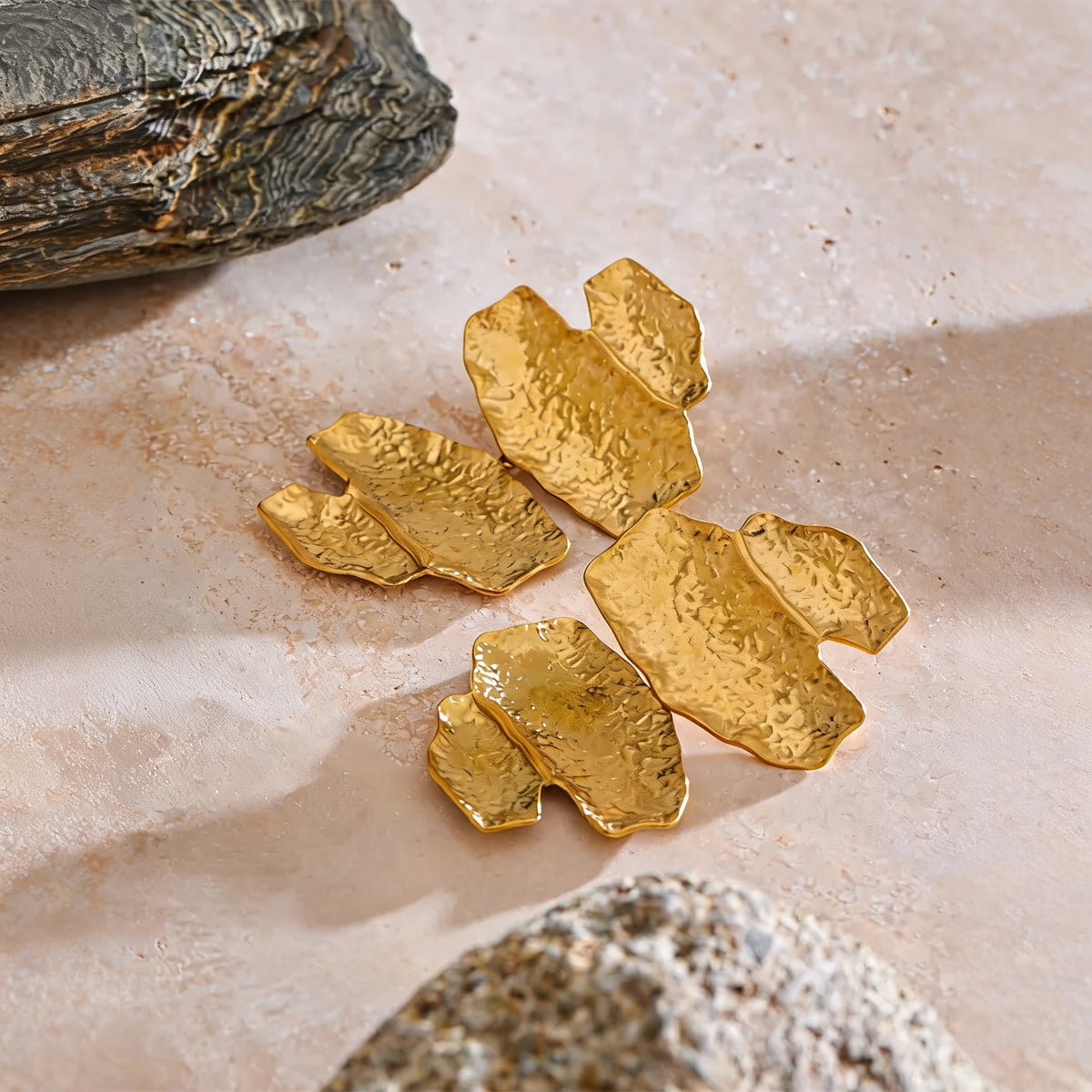 Faye hammered gold-tone drop earrings styled on warm travertine stone