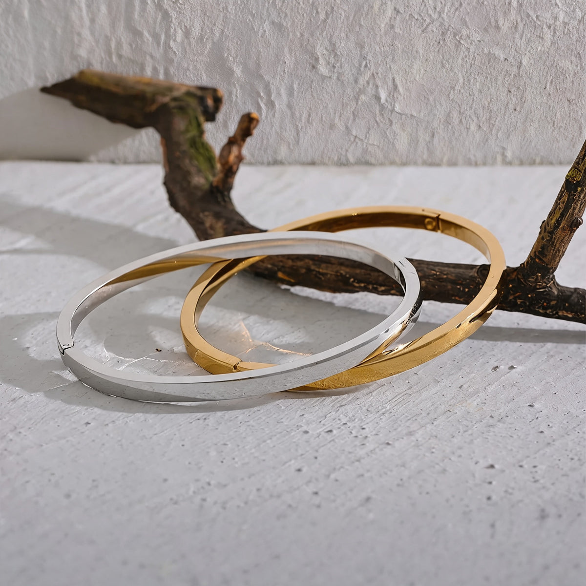 Gold and silver Rowan smooth bangles resting on a white plaster surface