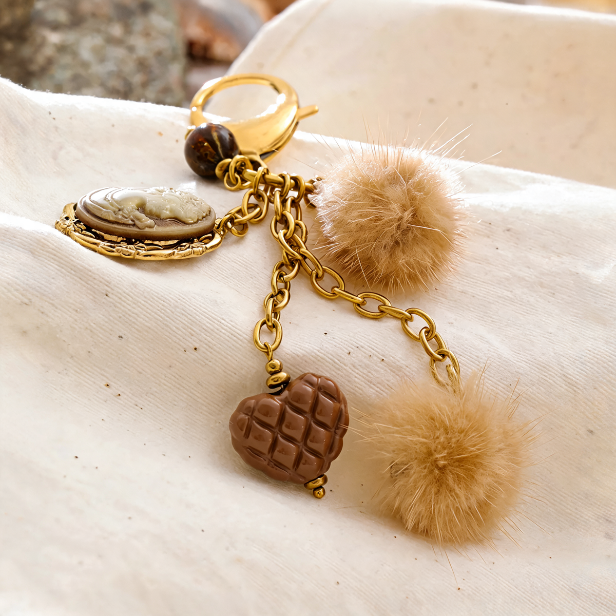 Posy Heart Portrait Keychain in Camel - gold-plated charm keychain with resin cameo, quilted heart and faux fur poms - draped on a cream fabric bag