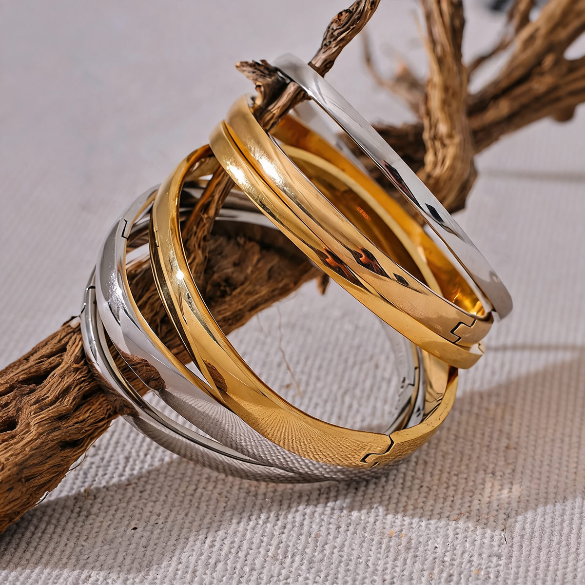Rowan smooth bangles in gold and silver stacked on driftwood over natural linen