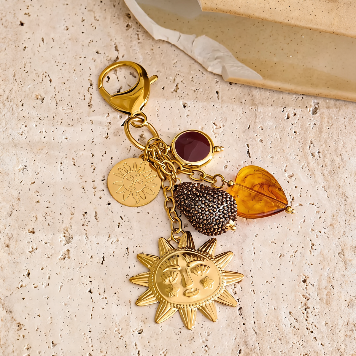 Marigold sun charm keychain laid on travertine beside a cream dish