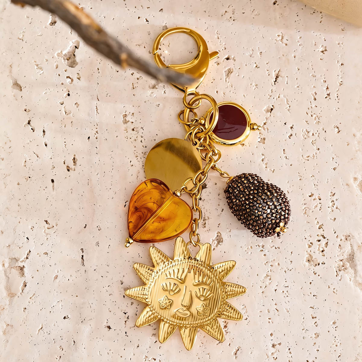 Marigold sun charm keychain on travertine with a dried branch