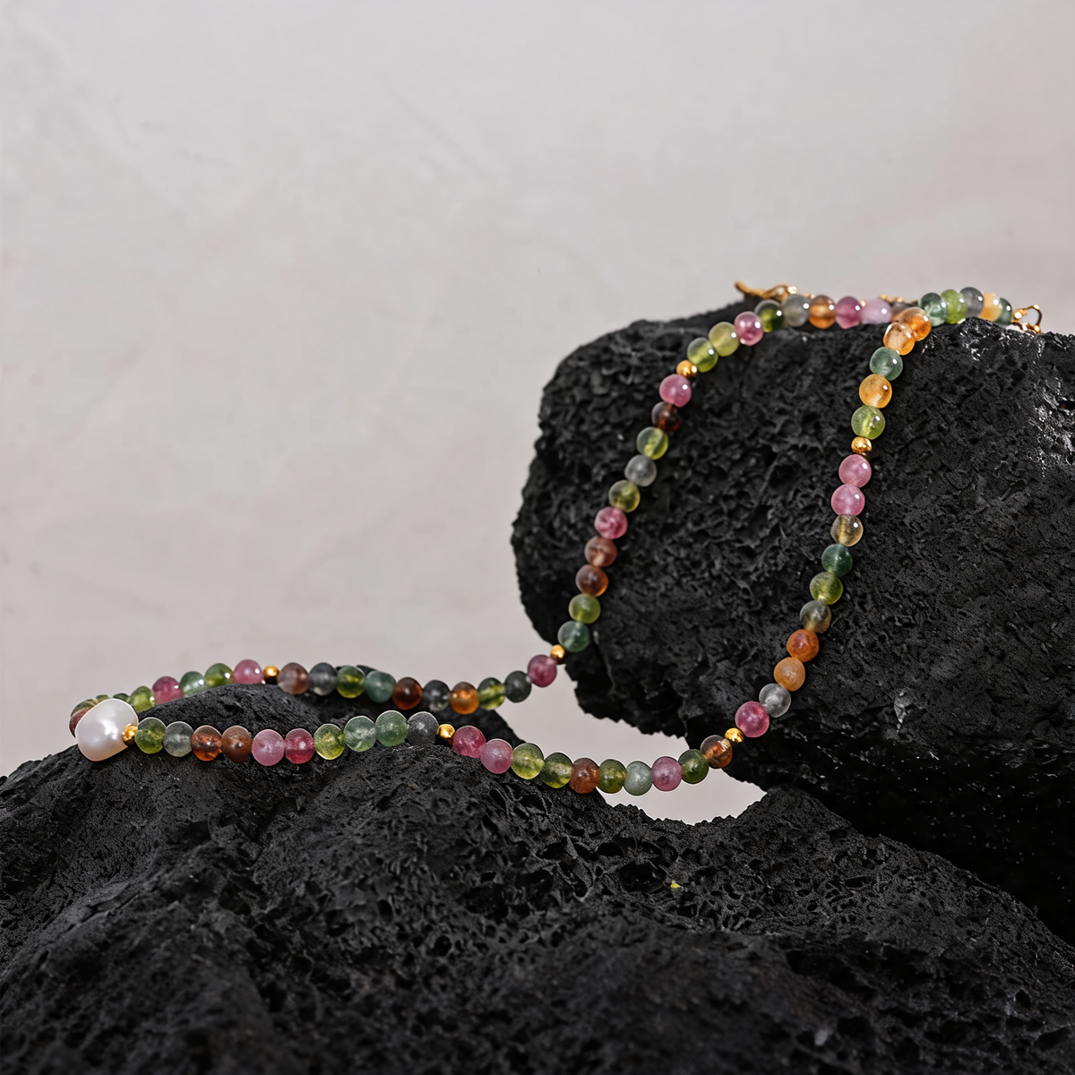Multicolor tourmaline bead necklace with a freshwater pearl draped over black lava rock