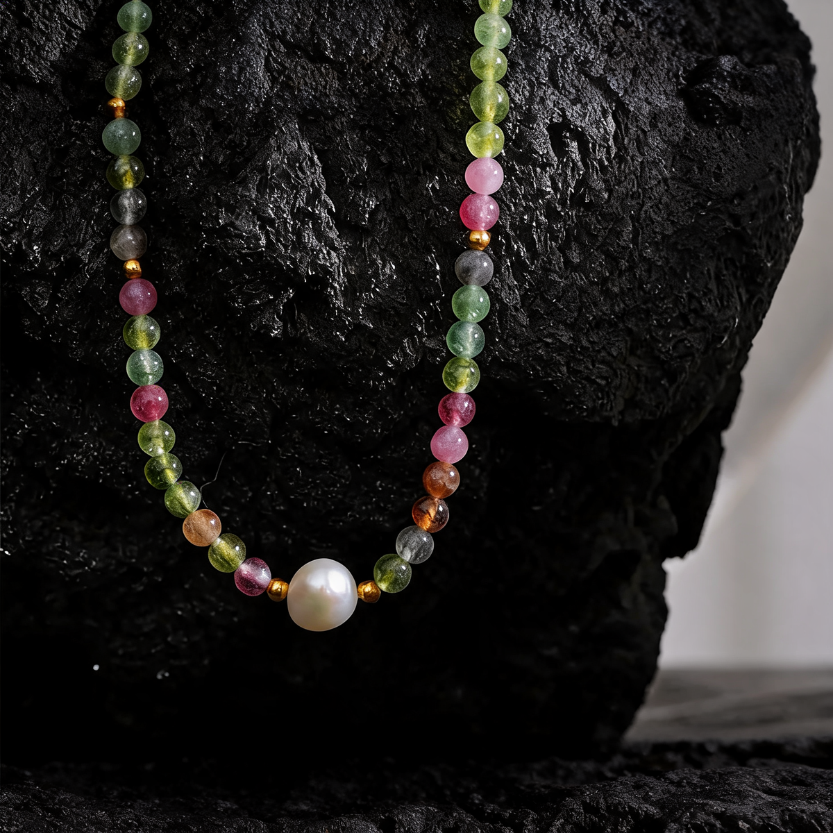 Close-up of the tourmaline beads and freshwater pearl against black lava rock