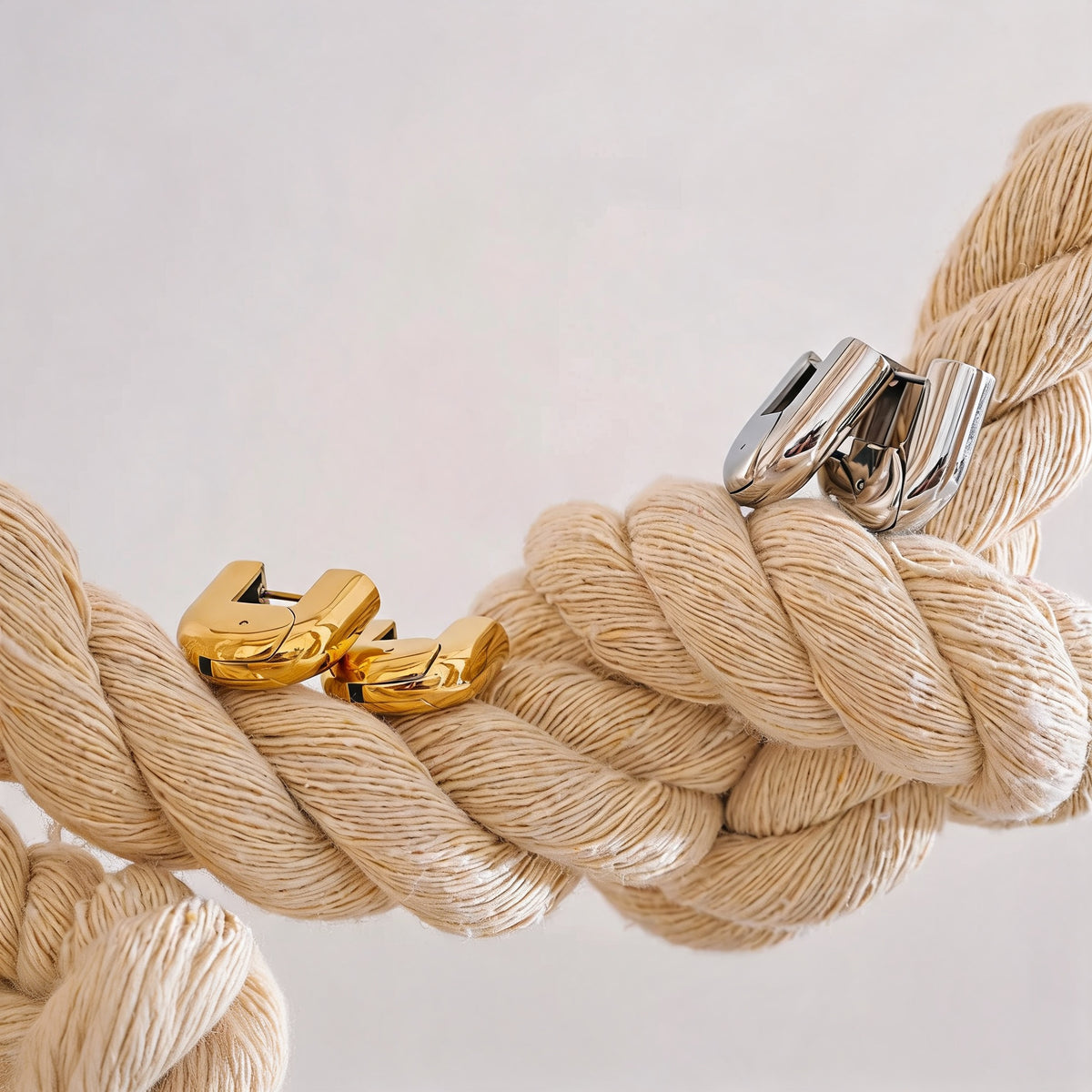Gold and silver Piper hollow hoop earrings resting on a cream rope