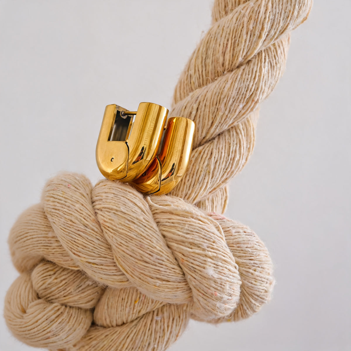 Gold Piper hollow hoop earrings nested on a cream rope