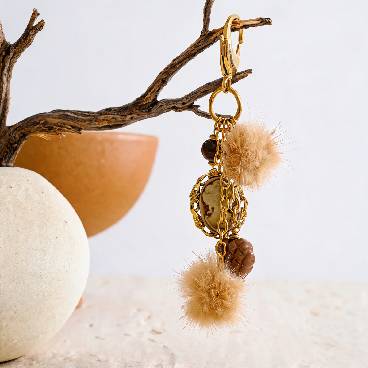 Posy Heart Portrait Keychain in Camel - gold-plated charm keychain with resin cameo, quilted heart and faux fur poms - hung from a driftwood branch