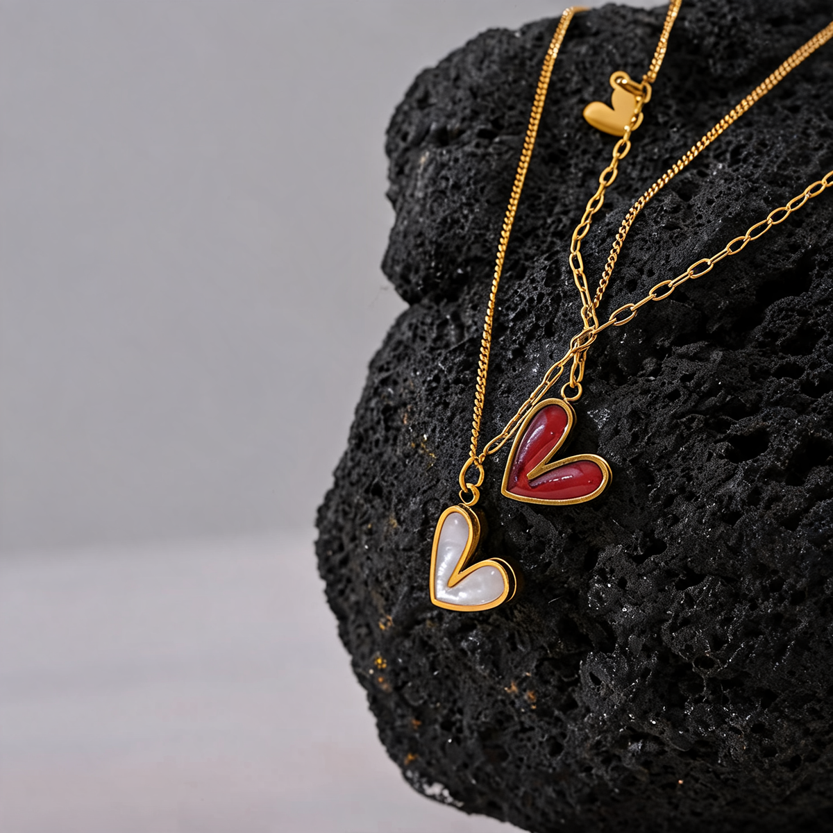 Rosa heart necklaces in red enamel and white shell draped over black lava rock