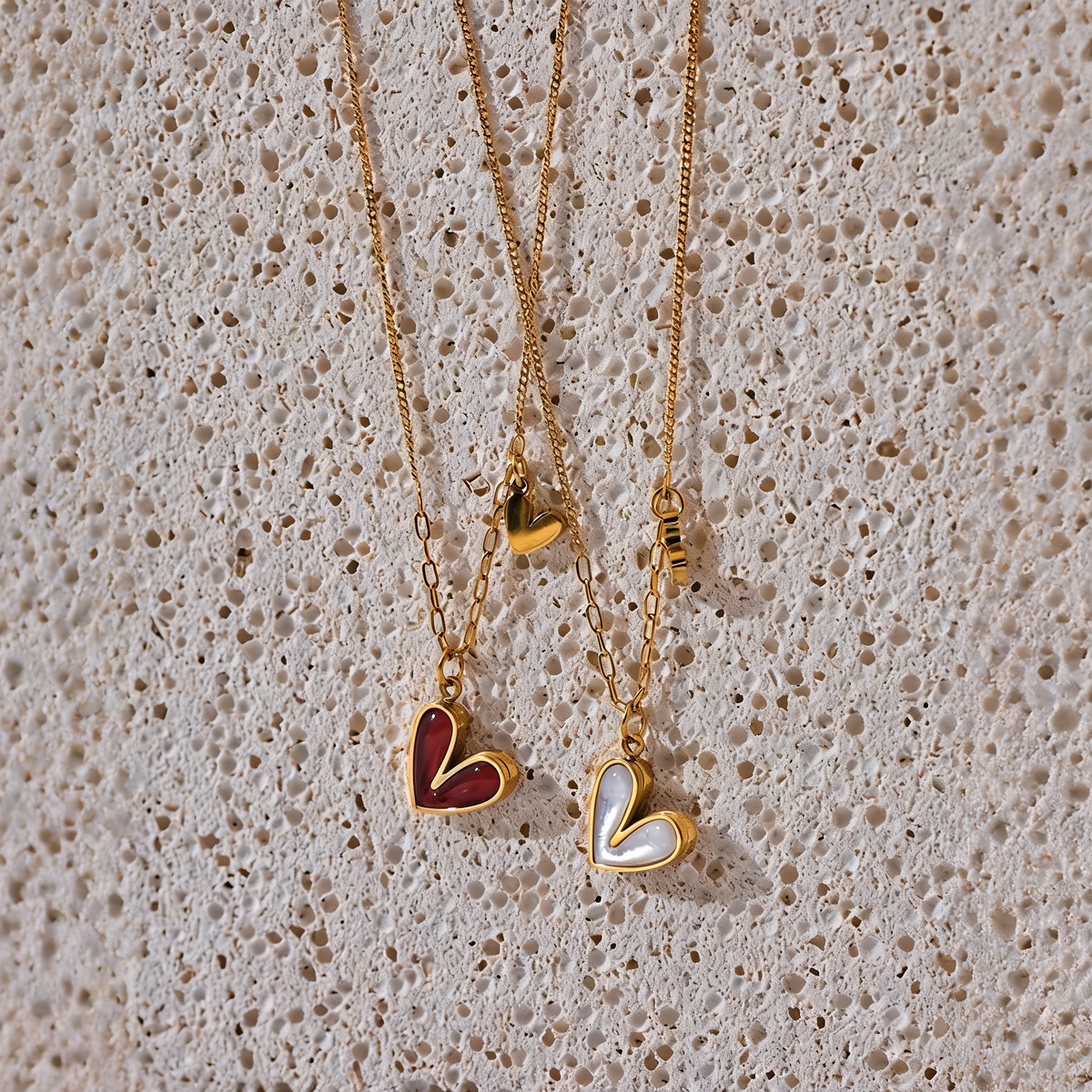 Rosa heart necklaces in red enamel and white shell on warm travertine stone