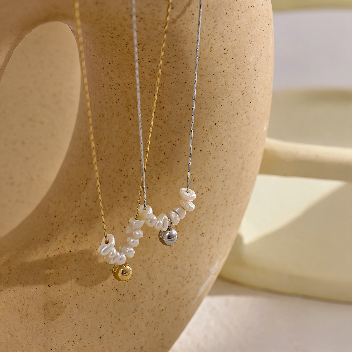 Gold and silver pearl bead necklaces draped over a warm terracotta vase